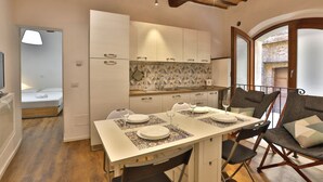 A compact kitchen with white cabinets, a tiled backsplash, and a dining area with a table set for two. - Independent apartment near Piazza del Campo (Siena)