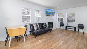 Un salon avec un plancher en bois, un canapé en cuir noir, une table à manger en bois avec des chaises et une cheminée.