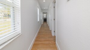 Un couloir étroit aux murs blancs et au plancher en bois, qui mène à une porte au fond.
