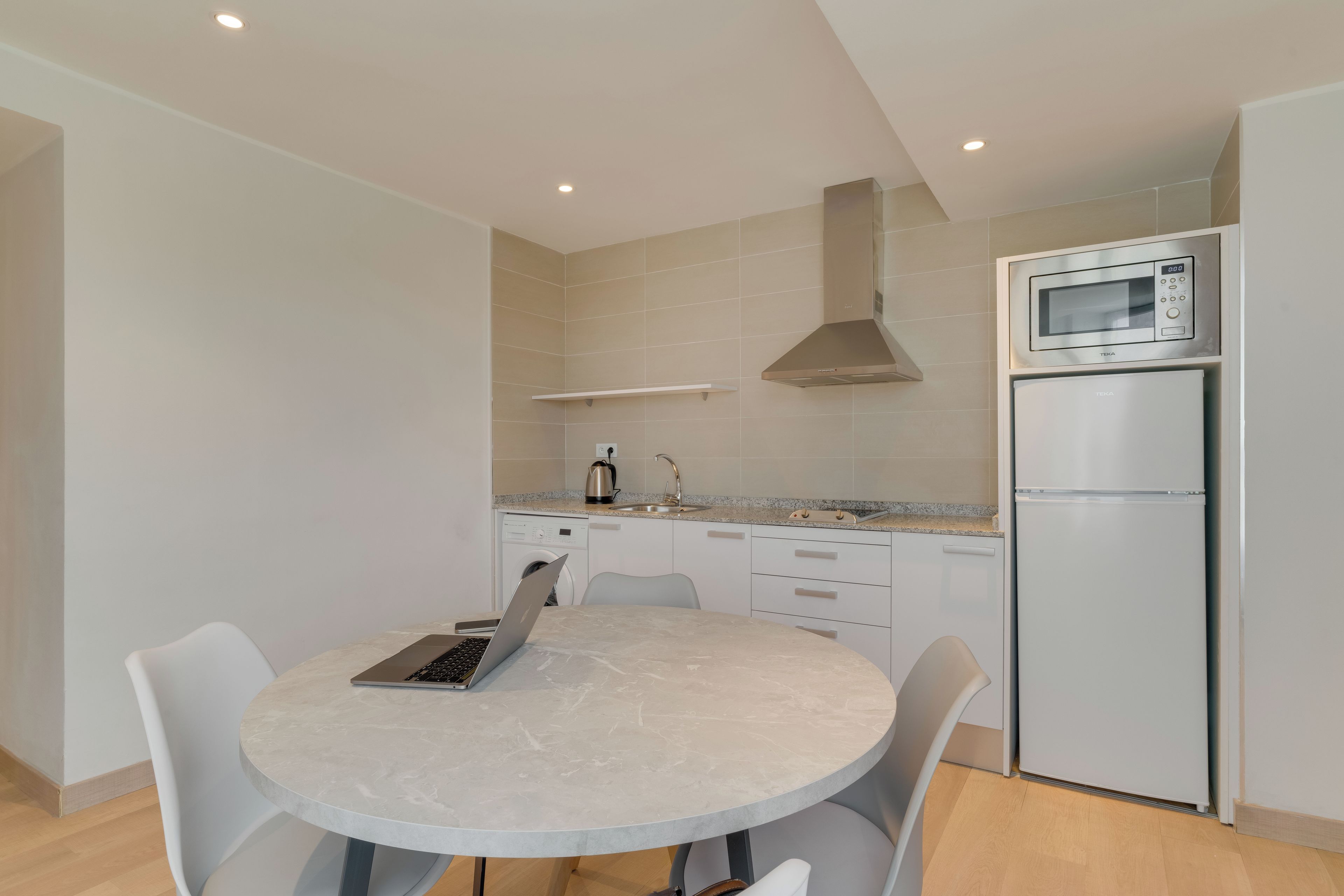 Una cocina moderna con una mesa redonda para comer, un microondas integrado y un refrigerador de acero inoxidable.