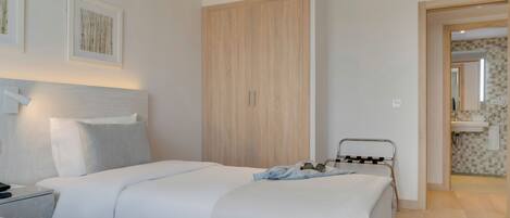 A modern bedroom with two beds, a wooden wardrobe, and a bathroom visible through an open door.