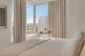 A hotel room with a large window, a bed, a small table with breakfast items, and curtains.