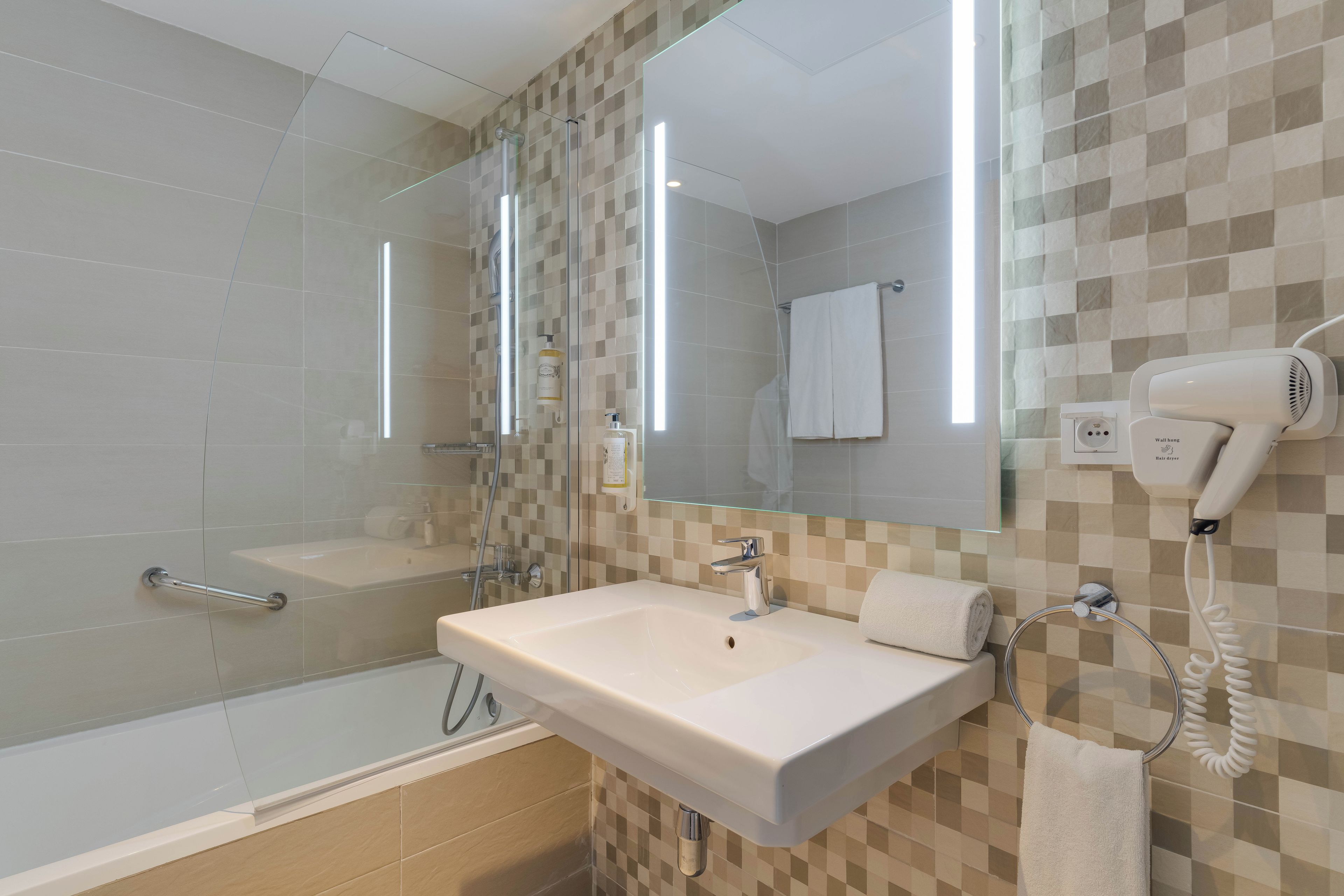 Un baño moderno con cabina de ducha de vidrio, un lavamanos blanco y un secador de pelo montado en la pared.