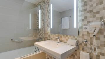 Un baño moderno con cabina de ducha de vidrio, un lavamanos blanco y un secador de pelo montado en la pared.