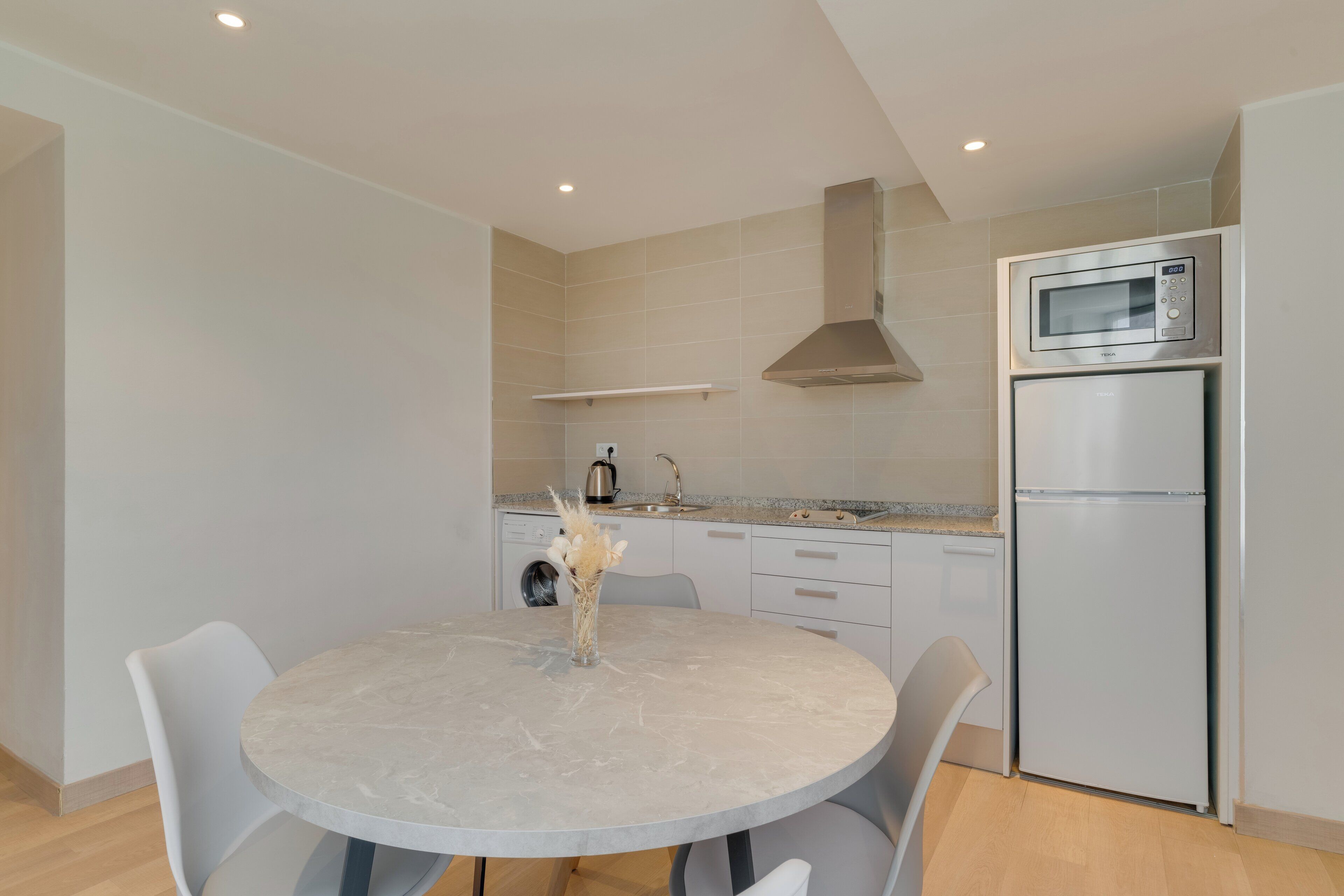 A modern kitchen with a round table, chairs, a built-in oven, microwave, and a washing machine.