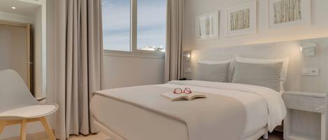 Une chambre à coucher moderne avec un grand lit, une table de chevet, une chaise et une fenêtre avec des rideaux.