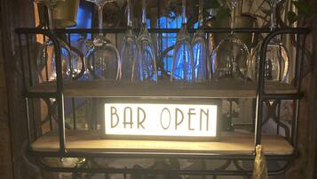 A bar area with a 'BAR OPEN' sign, shelves with wine glasses, and potted plants.
