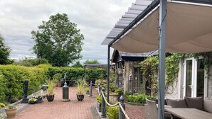 A covered patio area with a brick pathway, outdoor seating, and potted plants.