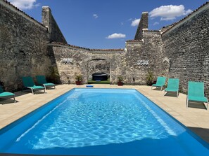 Piscina con paredes de piedra y sillas de descanso verdes.
