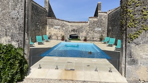 Ein Poolbereich mit Steinmauern, einem klaren blauen Pool und mehreren Liegestühlen.