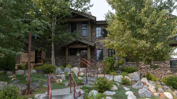 A two-story house with a stone facade, a stone staircase with metal railings, and a well-maintained garden with large rocks and greenery. - Grand View 3330: Top Floor Condo w/ Spectacular Teton Views- Air Conditioned! (Jackson)