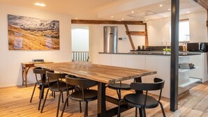 A modern kitchen with a wooden dining table and chairs, a large painting on the wall, and a view of the mountains. - Spacious Duplex Close to all Cultural Sites (Brussel)