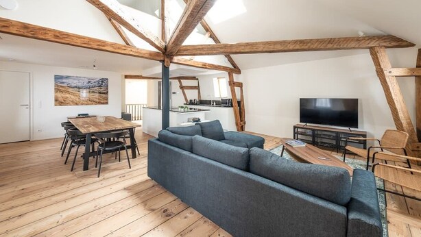 A spacious living area with a wooden ceiling, a large sofa, a dining table, and a television. - Spacious Duplex Close to all Cultural Sites (Brussel)