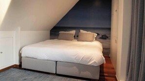 Ein Schlafzimmer mit Bett, Kissen und Blick auf das Meer durch eine geneigte Decke.