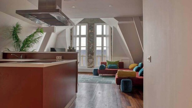 Eine moderne Küche mit einer zentralen Kochinsel, einem Essbereich mit einem roten Sofa und einem großen Fenster, das für natürliches Licht sorgt.