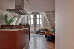 A modern kitchen with a central island, a dining area with a red sofa, and a large window providing natural light.