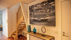 Eine Treppe führt zu einer Empore mit einem Vintage-Auto-Poster, einem Konsolentisch mit Dekoration und einer Tür.