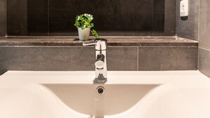 Une salle de bain moderne avec un lavabo blanc, un robinet chromé et une petite plante en pot posée sur le comptoir.