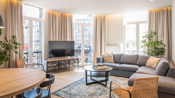 Un salon moderne avec un canapé, un téléviseur, une table à manger et un balcon agrémenté de rideaux.