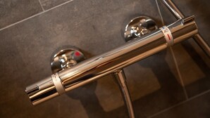 Une poignée de douche en métal, dotée d’un bouton de réglage de la température et d’un indicateur de débit d’eau.