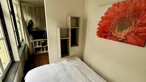 Ein Schlafzimmer mit Bett, Fenster, einer Holzregal und einem großen, roten Blumenbild an der Wand.
