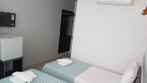 Una habitación de hotel pequeña con dos camas individuales, un escritorio con una impresora, un espejo y un aire acondicionado de pared.