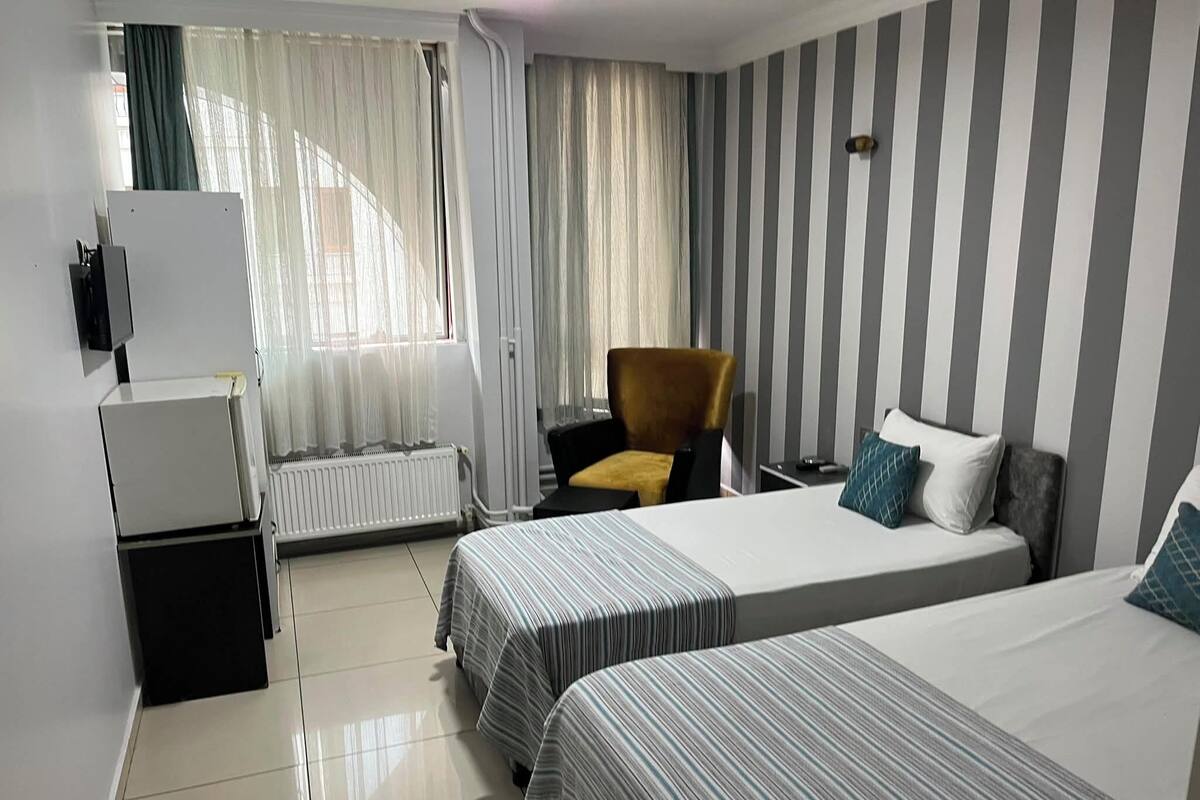 Habitación de hotel con dos camas, una silla, un escritorio, un radiador y una ventana con cortinas.