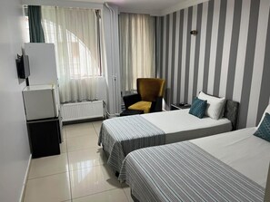 A hotel room with two beds, a chair, a desk, a radiator, and a window with curtains. - Lotus Otel (Konya)