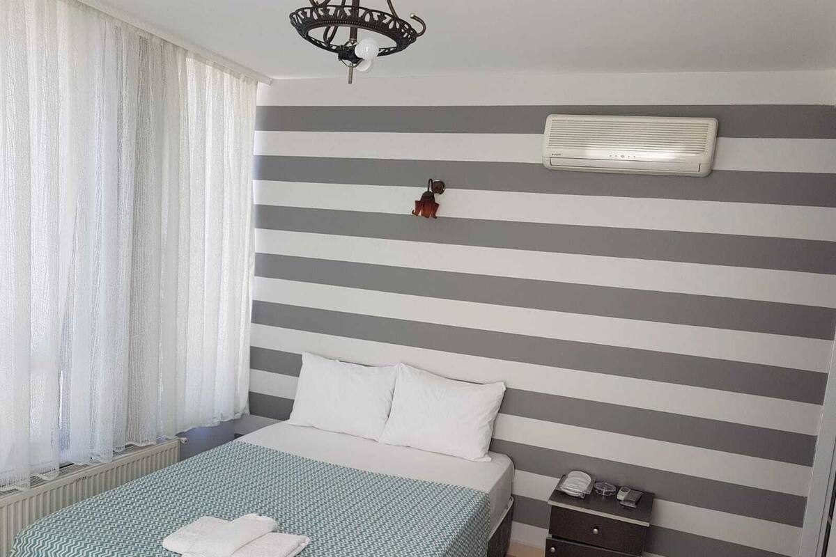 Habitación de hotel con cama, mesita de noche, aire acondicionado de pared y ventana con cortinas.