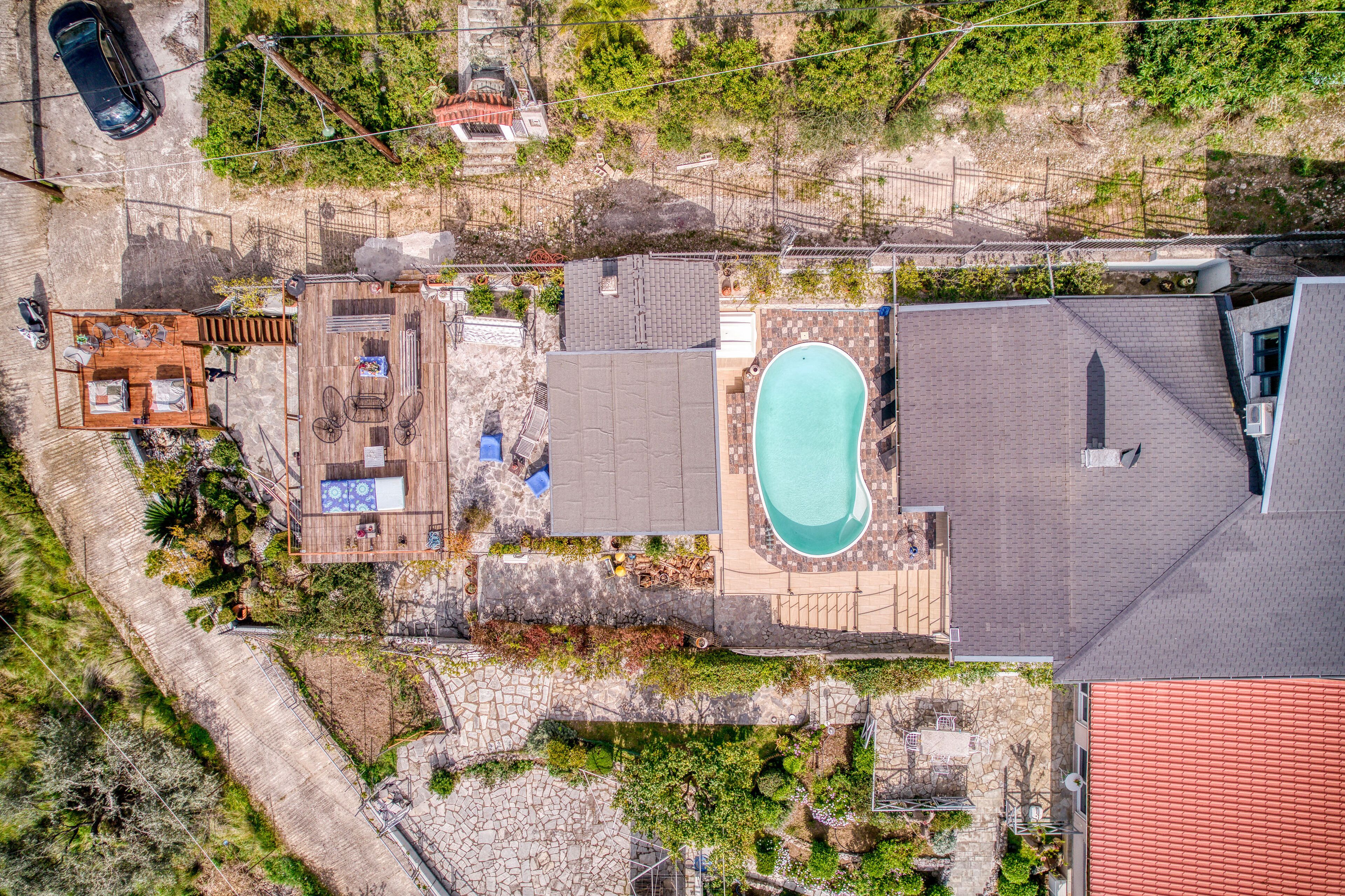 An aerial view of a residential property with a swimming pool, patio area, and a small deck.