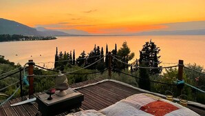 Une terrasse en bois offrant une vue sur un lac et des montagnes au coucher du soleil.