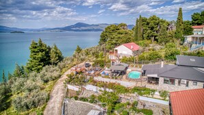 Une propriété située sur la côte, dotée d’une piscine, d’une maison à toit rouge et offrant une vue sur la mer et les montagnes.