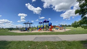 Un parque infantil con toboganes y estructuras para escalar, rodeado de césped y un cielo despejado.