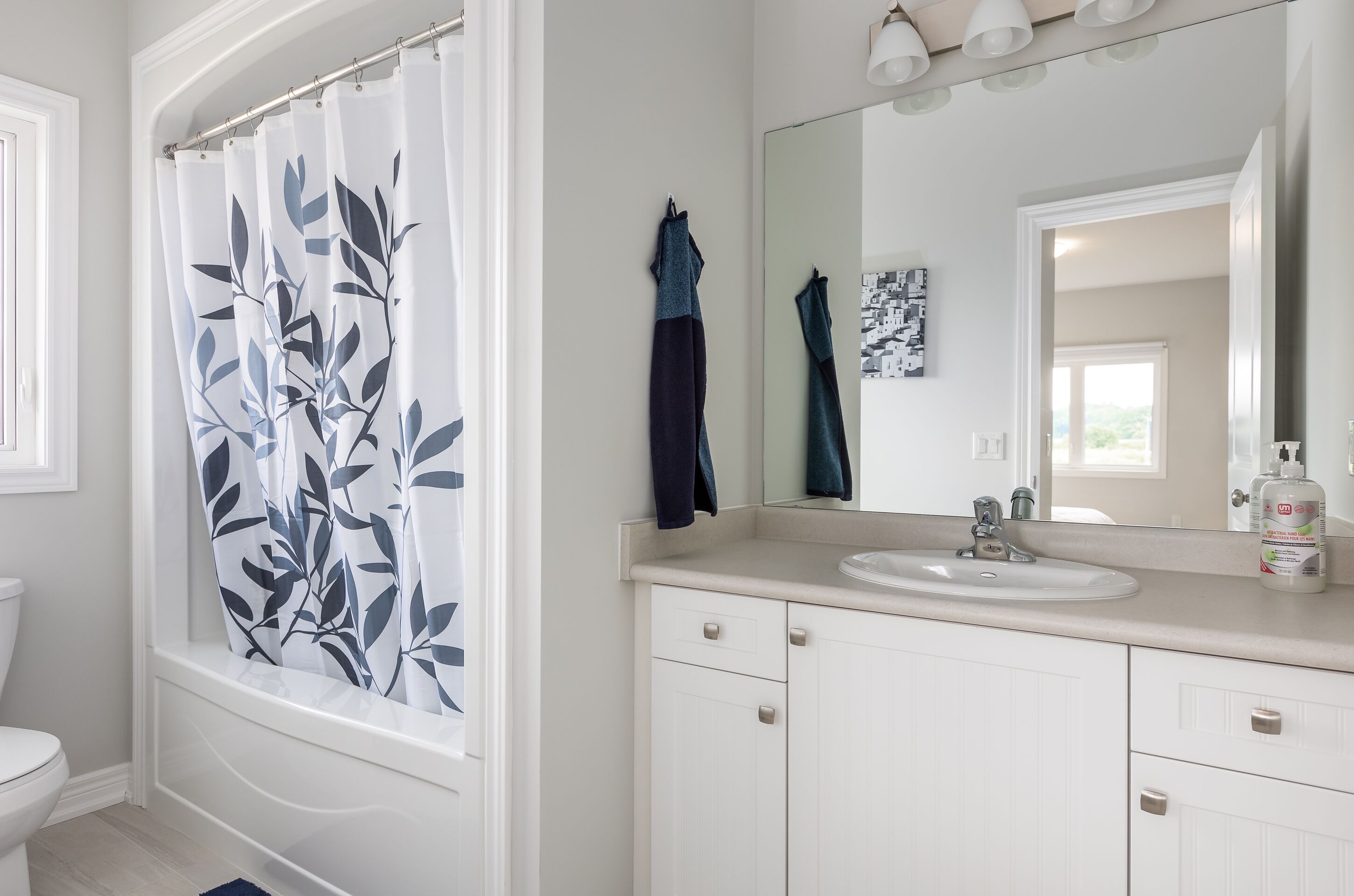 A bathroom with a white sink, a mirror, and a shower curtain with a leaf pattern.