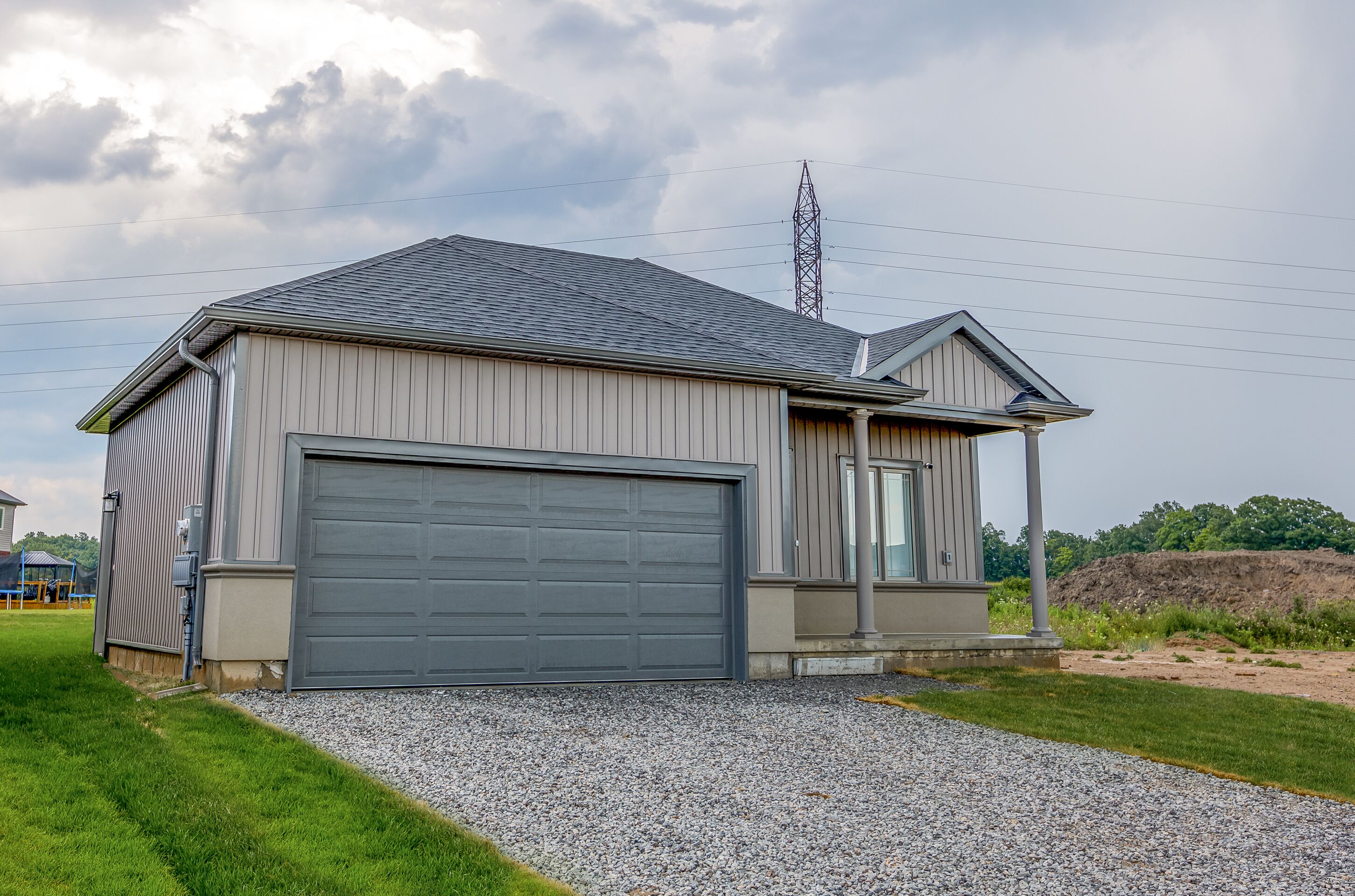 A single-story house with a grey garage door, a small porch, and a gravel driveway.