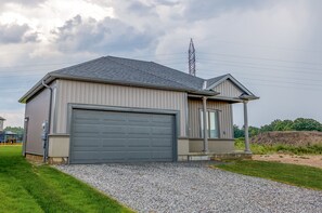 Une maison de plain-pied avec une porte de garage grise, un petit porche et une allée gravillonnée.
