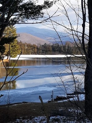 Une vue paisible sur un lac, avec une jetée en bois s’avançant dans l’eau, entourée d’arbres et de montagnes en arrière-plan.