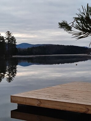 A wooden dock extending into calm water, surrounded by trees and a distant mountain range. - Adirondack Hideout, lakefront location and sandy shoreline (Lyon Mountain)