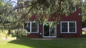 A red building with two large windows and a door, surrounded by a well-maintained lawn. - Adirondack Hideout, lakefront location and sandy shoreline (Lyon Mountain)