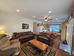 A living room with a sofa, armchair, and coffee table, a dining area with chairs and a table, and a kitchen with cabinets and appliances. - Adirondack Hideout, lakefront location and sandy shoreline (Lyon Mountain)