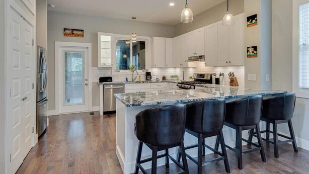 Una cocina moderna con armarios blancos, una isla grande con taburetes de bar e iluminación colgante.