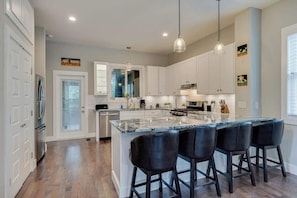 A modern kitchen with white cabinets, a large island with bar stools, and pendant lighting. - Spacious Home w/Game Room+Walk to Highland Yards (Nashville)