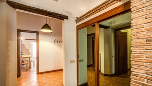 Ein Flur mit Fliesenboden, einer Pendelleuchte, einem Holzbalken an der Decke und einer Ziegelwand.