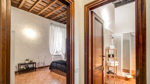 Ein Schlafzimmer mit einem Bett, einem Nachttisch, einem kleinen Tisch mit Lampe und einem Fenster mit Vorhängen.