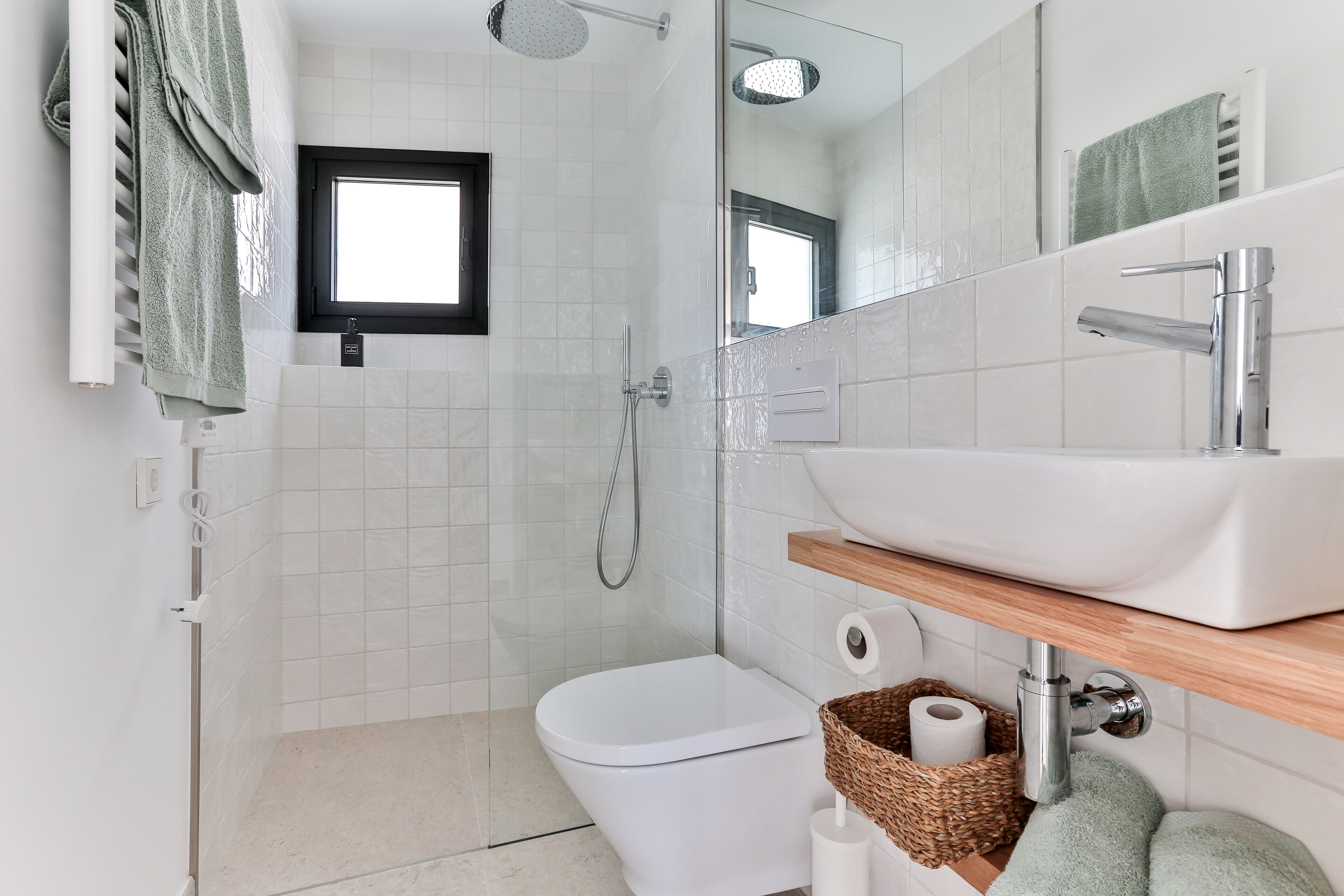Et moderne badeværelse med et hvidt toilet, bruser, spejl og en vask med en træhylde.