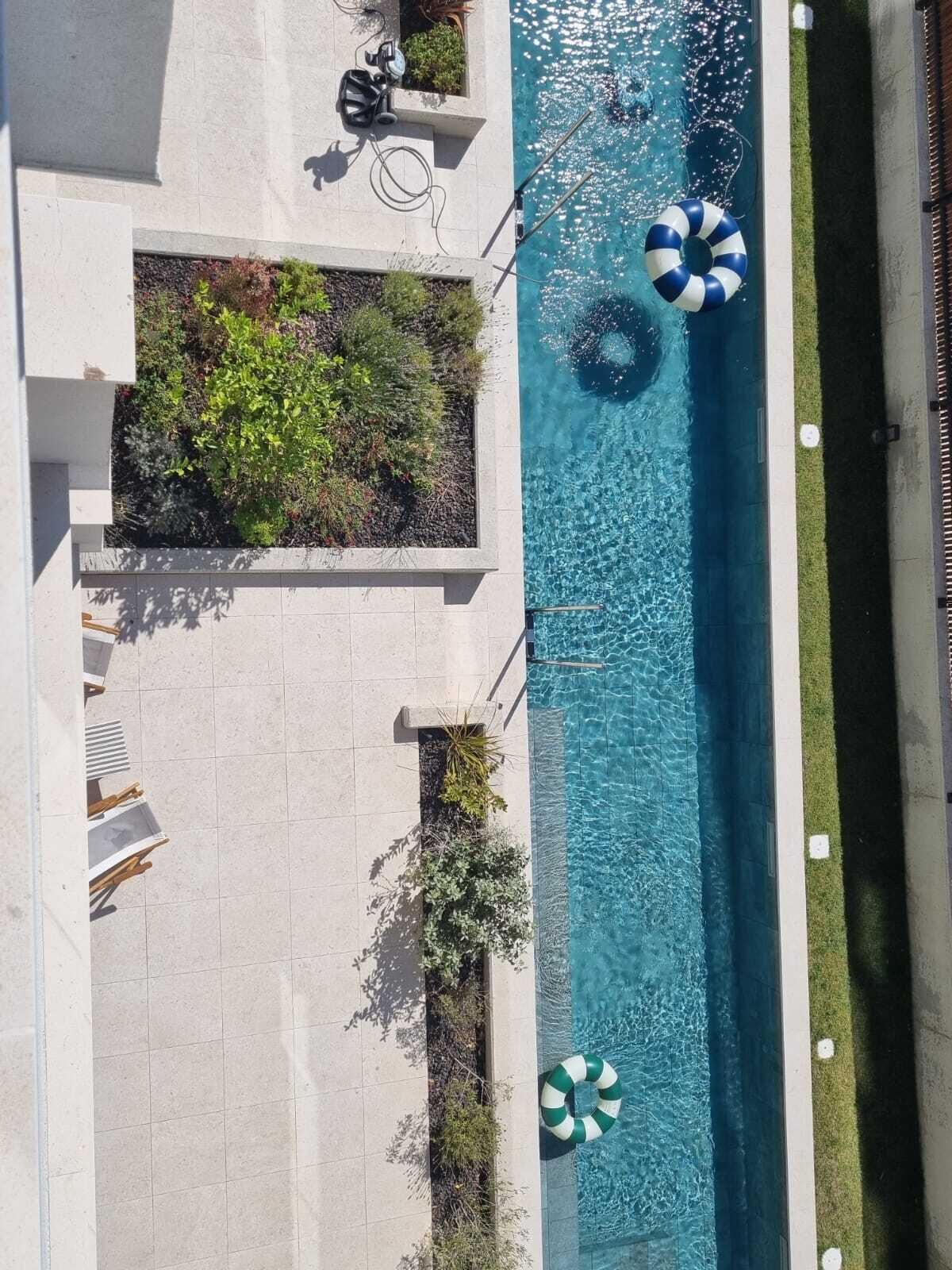 An aerial view of a swimming pool with a tiled deck, surrounded by greenery and two beach umbrellas.