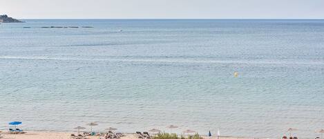 A beach with umbrellas, sun loungers, and a clear view of the sea.