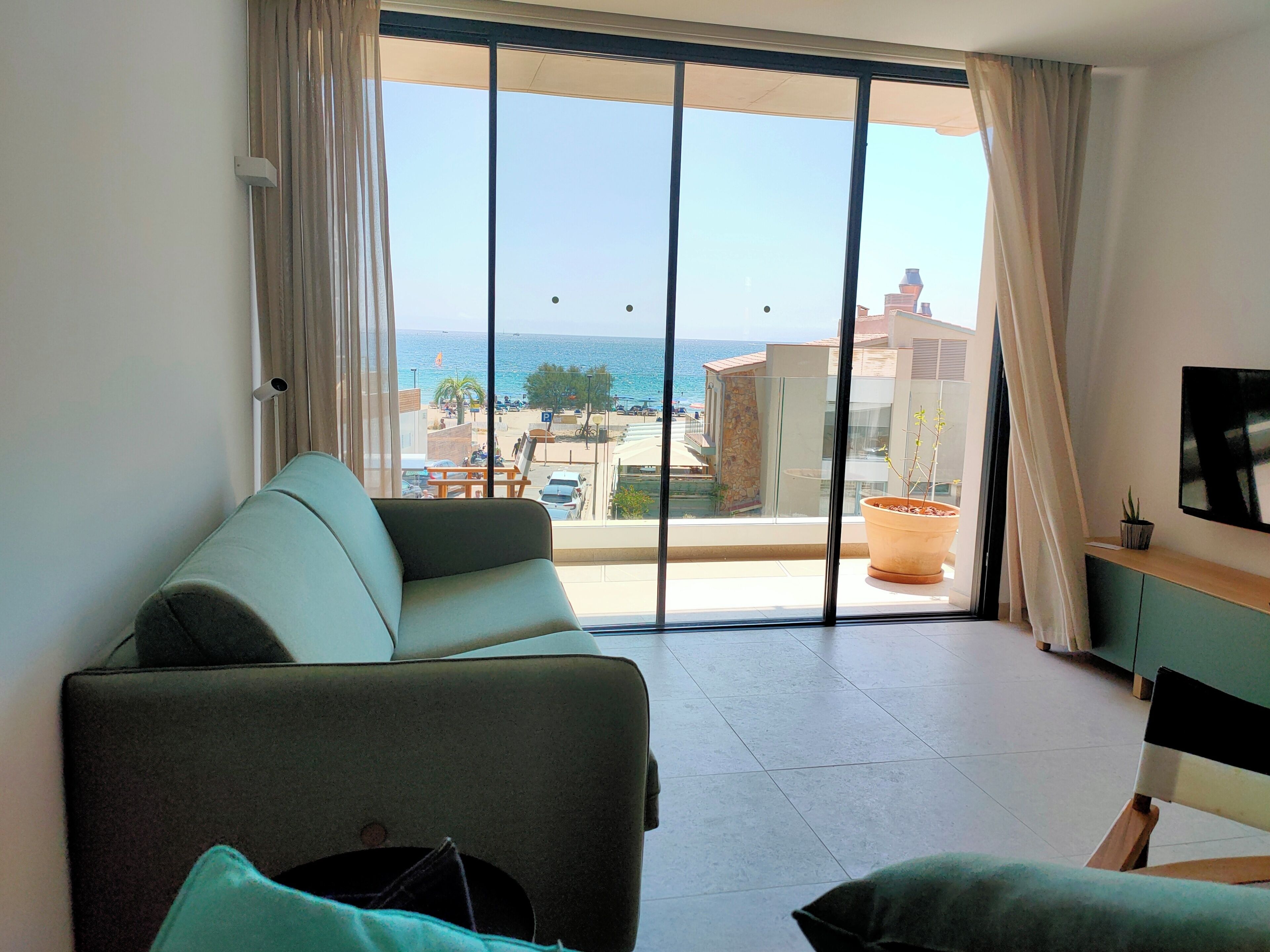 Uma sala de estar com sofá, televisão e vista para o mar e edifícios.
