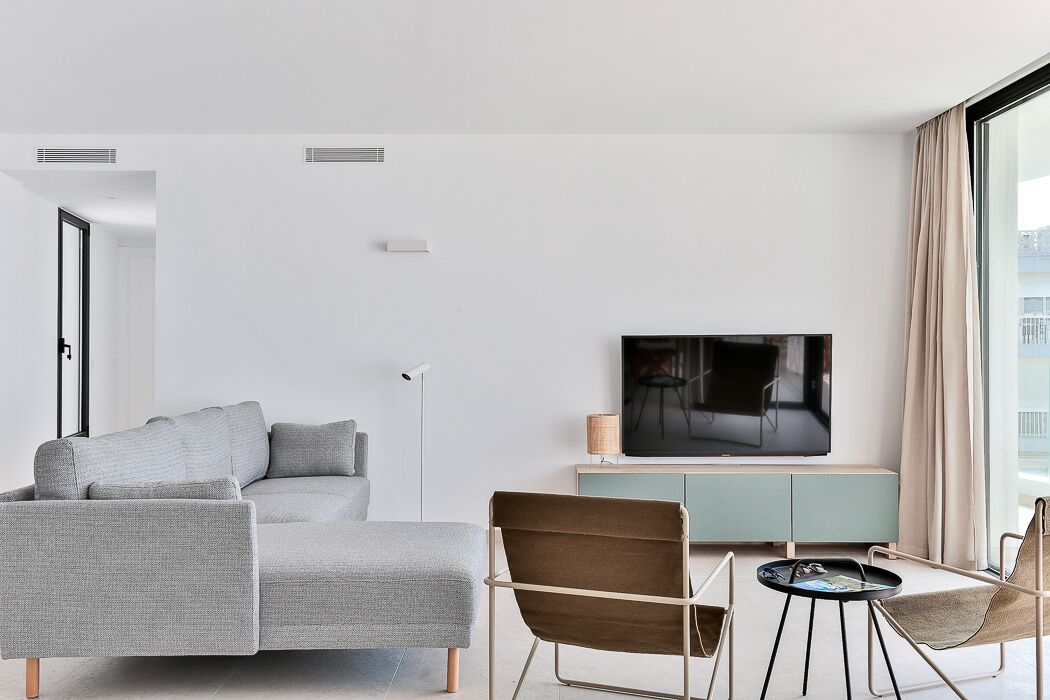 A modern living room with a grey sectional sofa, a brown armchair, a small round table, and a flat-screen TV on a light teal console.