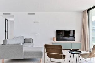 Una sala de estar moderna con un sofá seccional gris, un sillón marrón, una mesita redonda y un televisor de pantalla plana sobre un mueble de color verde agua.